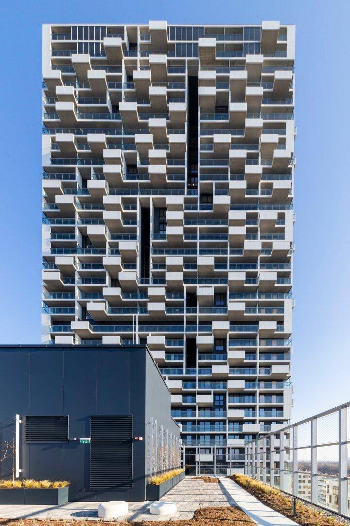 Detailansicht der modernen Hochhausfassade mit zahlreichen versetzten Balkonen unter blauem Himmel.