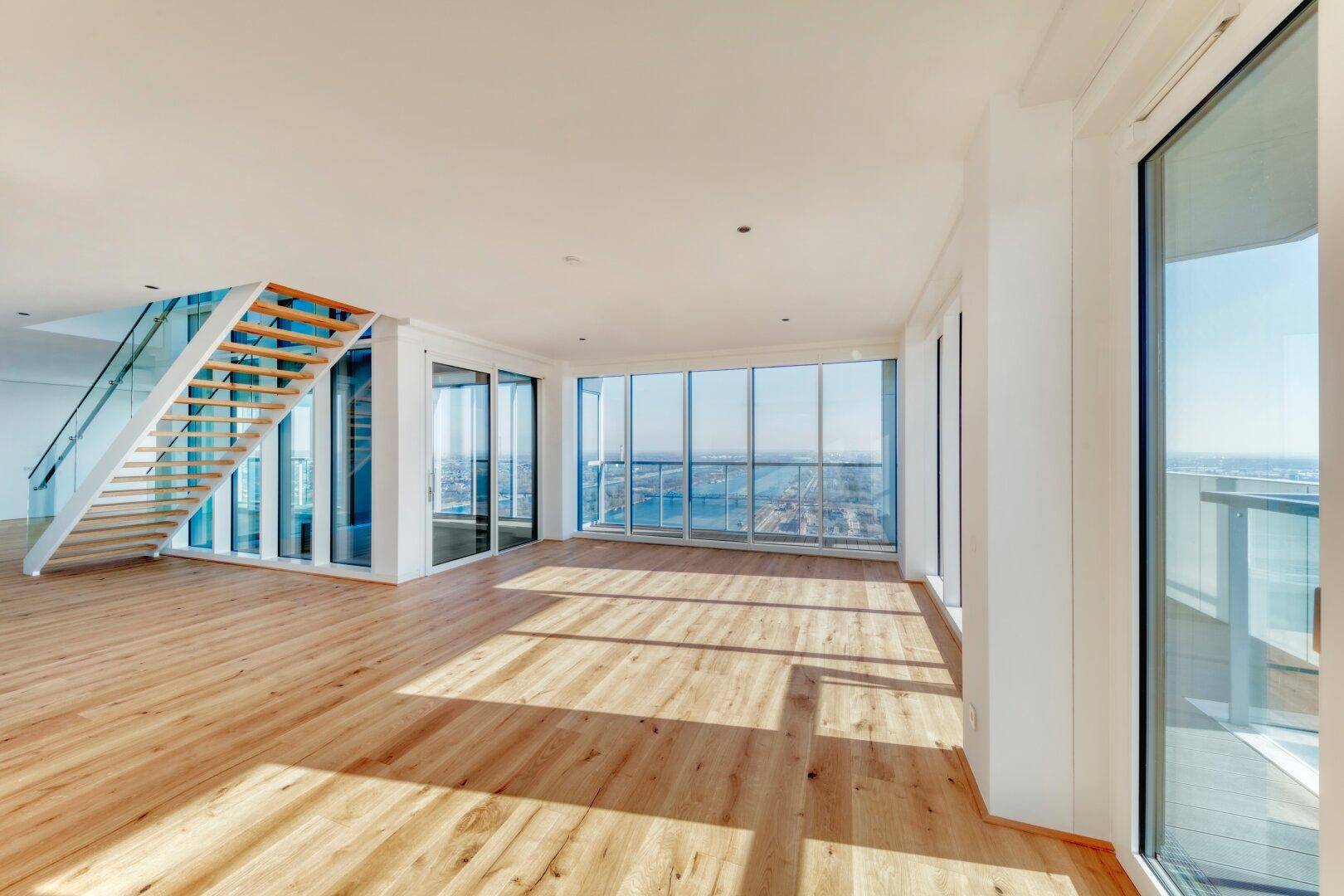 Geräumiges Wohnzimmer mit Holzboden, moderner Treppe und Panoramafenstern mit Blick auf die Stadt.