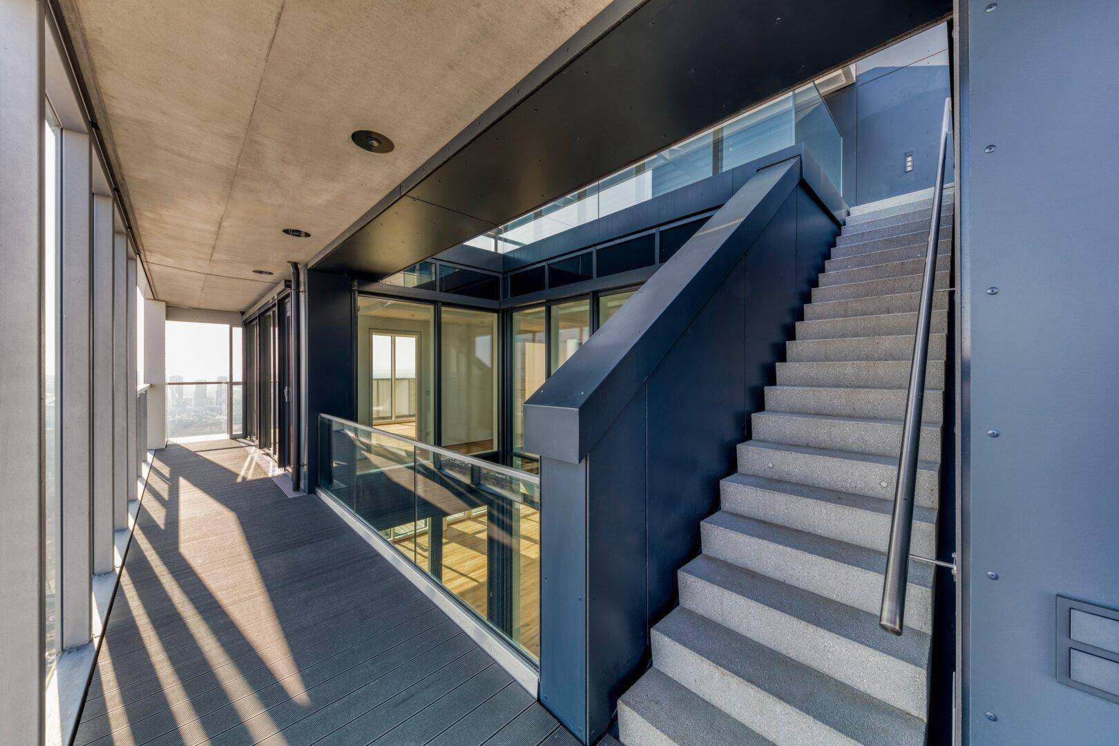 Moderner Außenbereich mit Treppe, Glasgeländer und Blick auf die Umgebung.