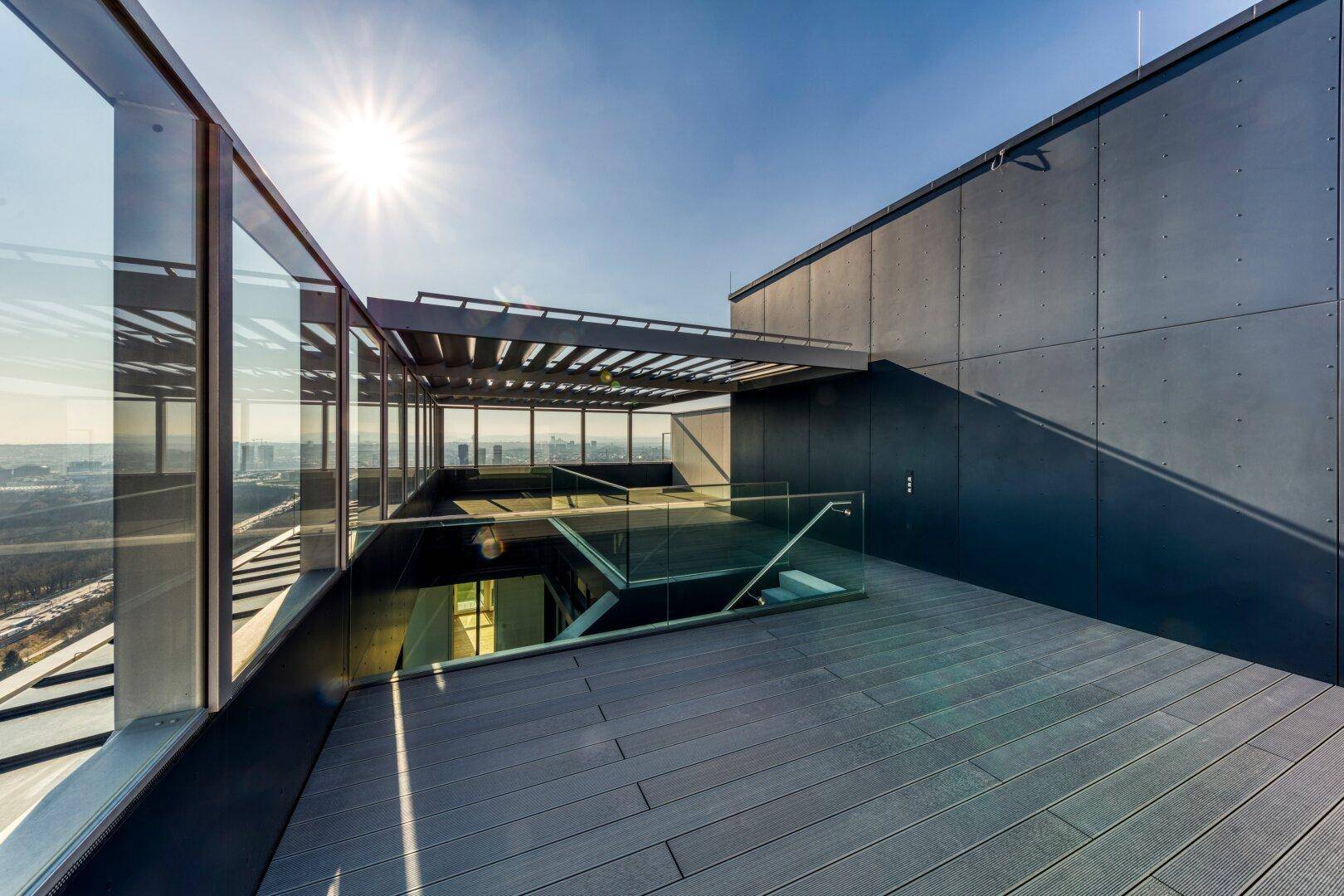 Große Dachterrasse mit Holzbelag, Glasgeländer und weitem Panoramablick.