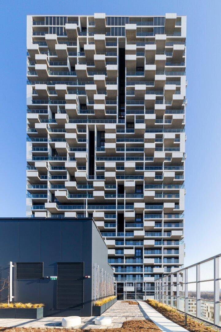 Moderne Hochhausfassade mit vielen versetzten Balkonen und Glasbrüstungen unter klarem Himmel.