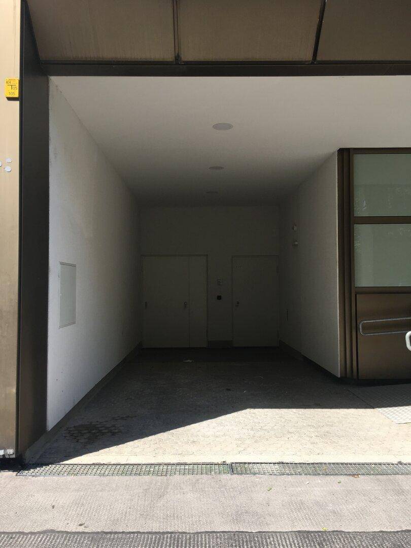 Eingangsbereich zu einer Tiefgarage oder einem überdachten Parkplatz mit Rampe und schlichten Wänden.