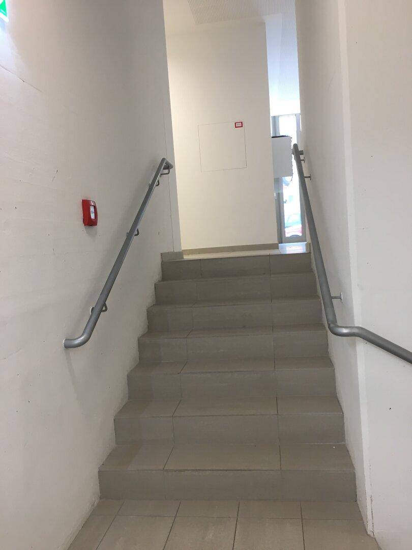 Treppenhaus mit Fliesenstufen und beidseitigen Handläufen, führt zu einem oberen Stockwerk.