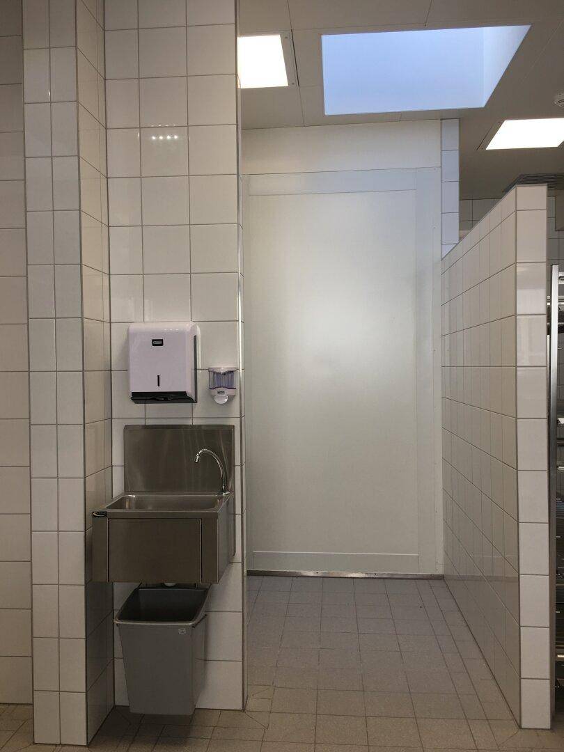 Waschbecken aus Edelstahl mit Seifenspender und Papierhandtuchhalter in einem gefliesten Raum.