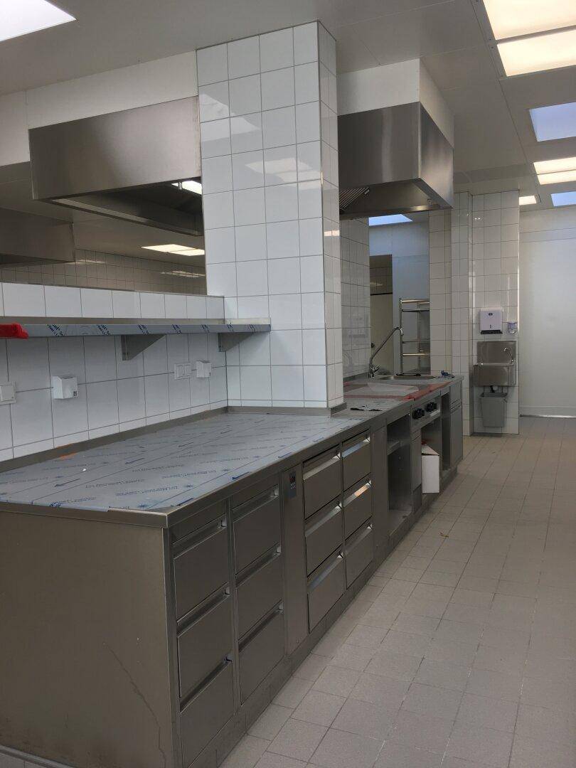 Lange Küchenzeile aus Edelstahl mit vielen Schubladen und Arbeitsflächen, geflieste Wände.