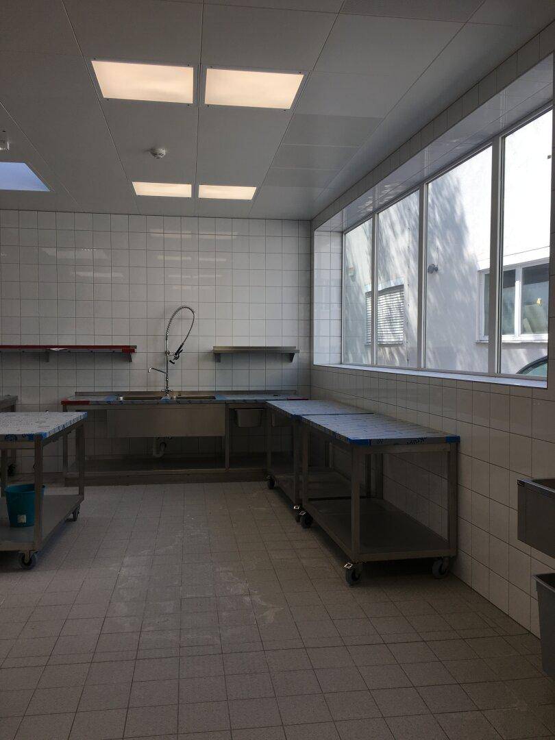Küchenzeile aus Edelstahl mit Spüle und Arbeitsflächen, große Fenster für natürliches Licht.