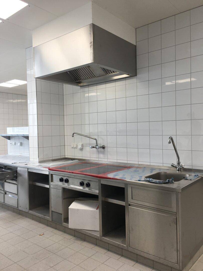 Küchenzeile aus Edelstahl mit Gaskochfeld, Spüle und Dunstabzugshaube, geflieste Wände.