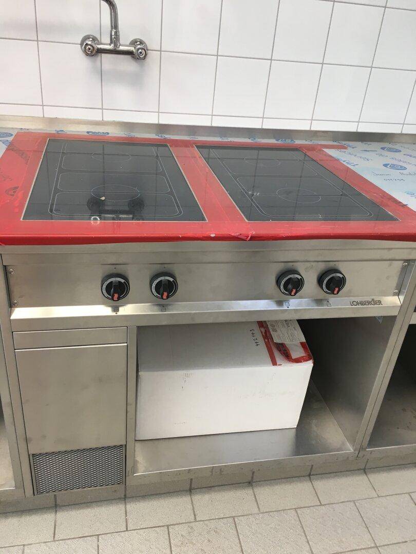 Nahaufnahme eines Induktionskochfeldes mit Bedienknöpfen in einer professionellen Edelstahlküche.