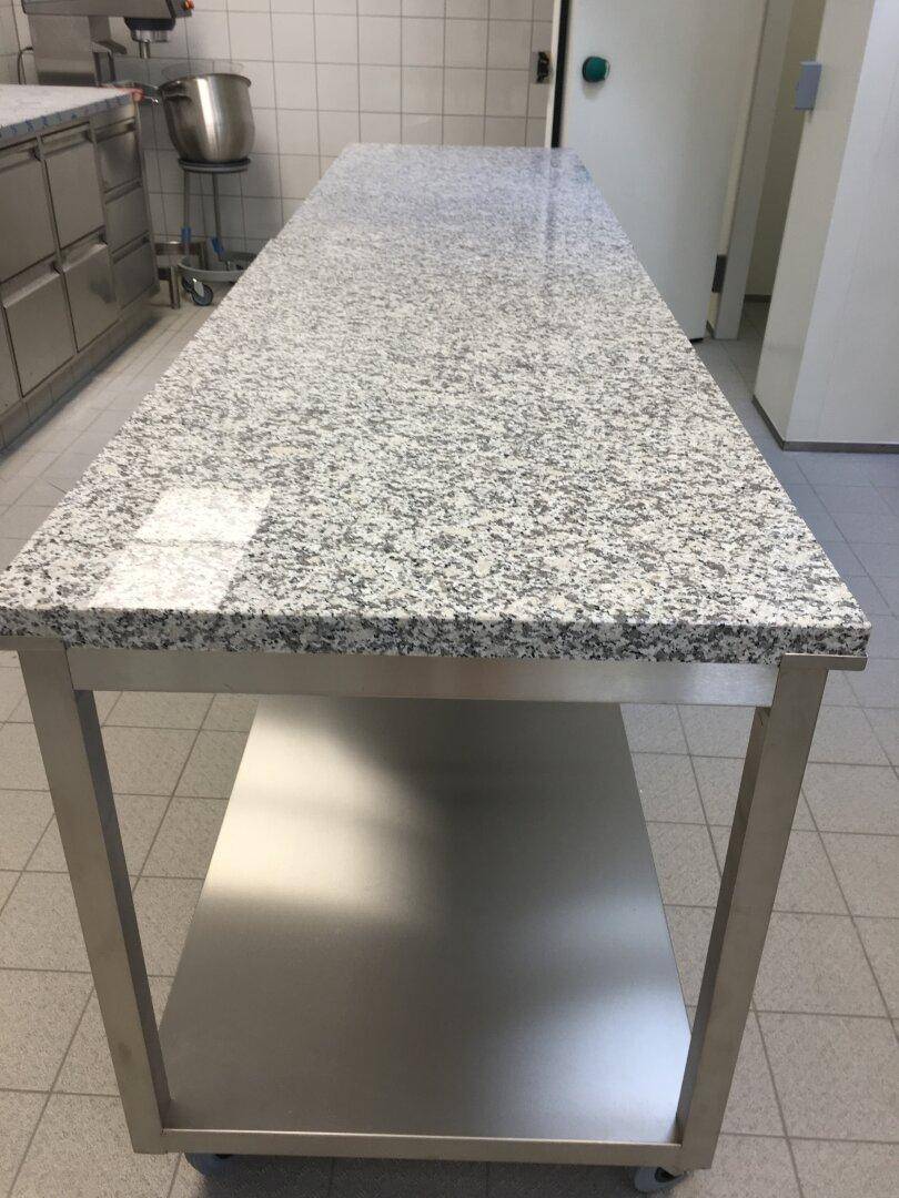 Mobile Kücheninsel mit Granit-Arbeitsplatte und Edelstahlgestell in einer gefliesten Gewerbeküche.