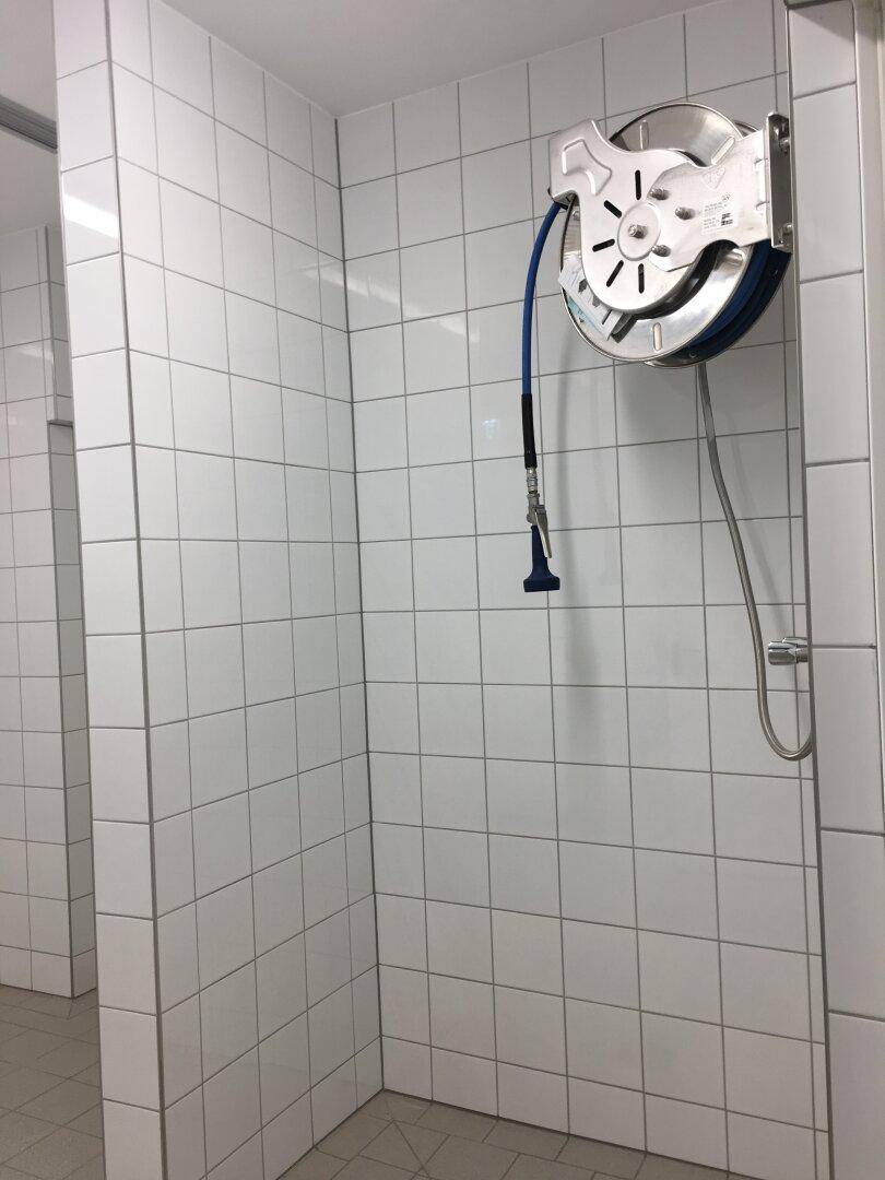 Wandmontierte Schlauchtrommel mit blauer Sprühdüse in einem gefliesten Bereich, bereit für die Reinigung.