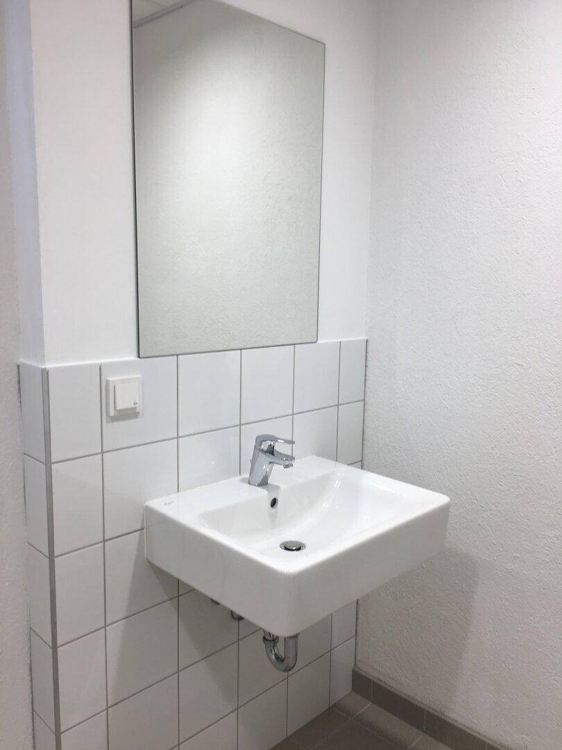 Modernes Waschbecken mit Spiegel und weißen Wandfliesen in einem schlichten Badezimmer.