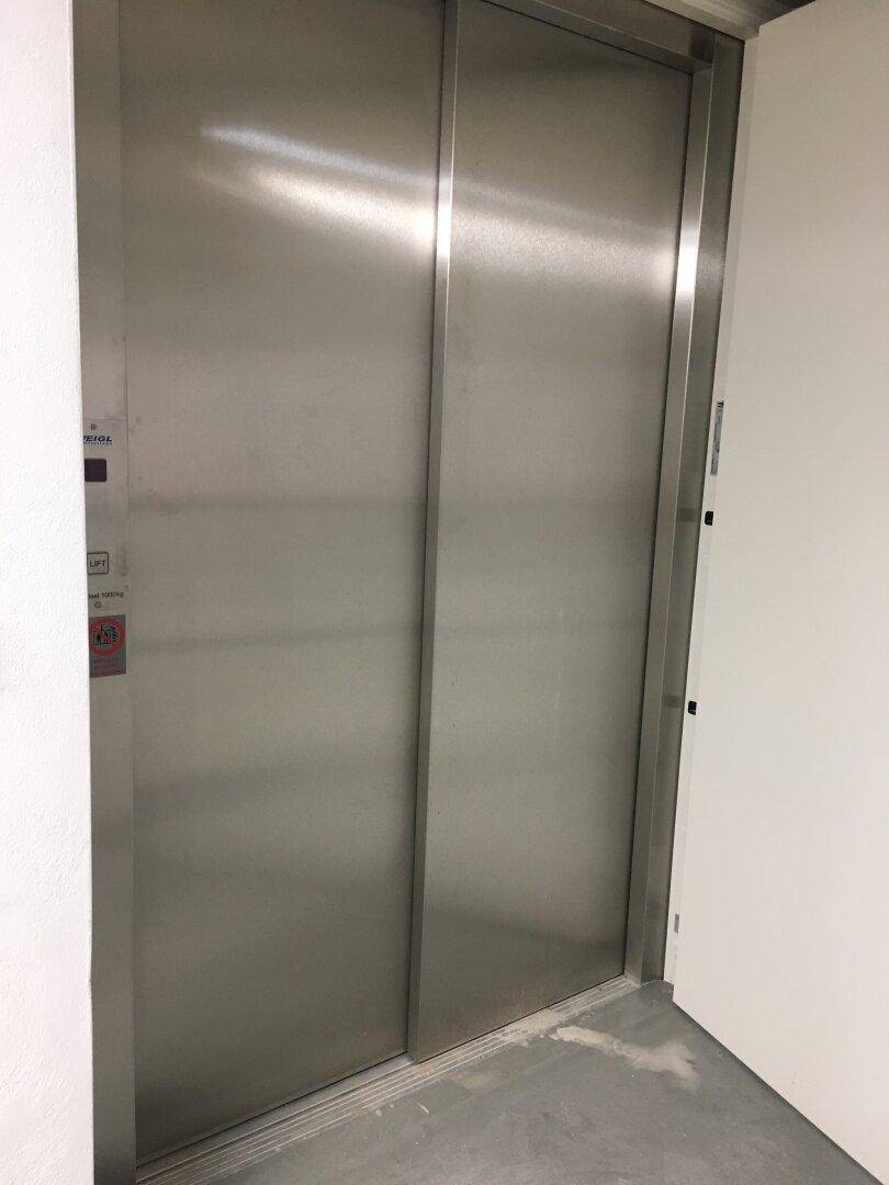 Moderne Aufzugstüren aus gebürstetem Edelstahl in einem hellen Flur.