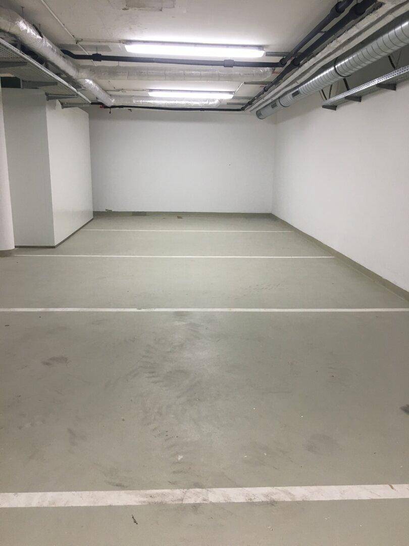 Mehrere leere Parkplätze in einer sauberen Tiefgarage mit weißen Wänden und Deckenbeleuchtung.