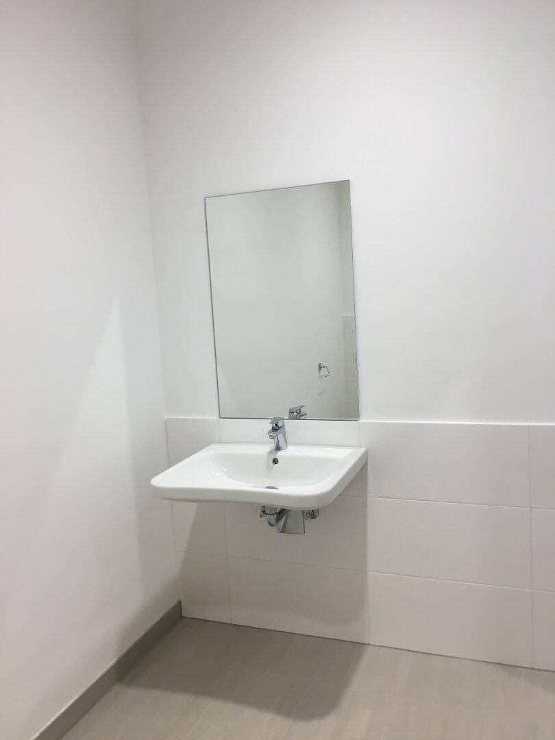 Modernes Waschbecken mit Spiegel und weißen Wandfliesen in einem schlichten Badezimmer.