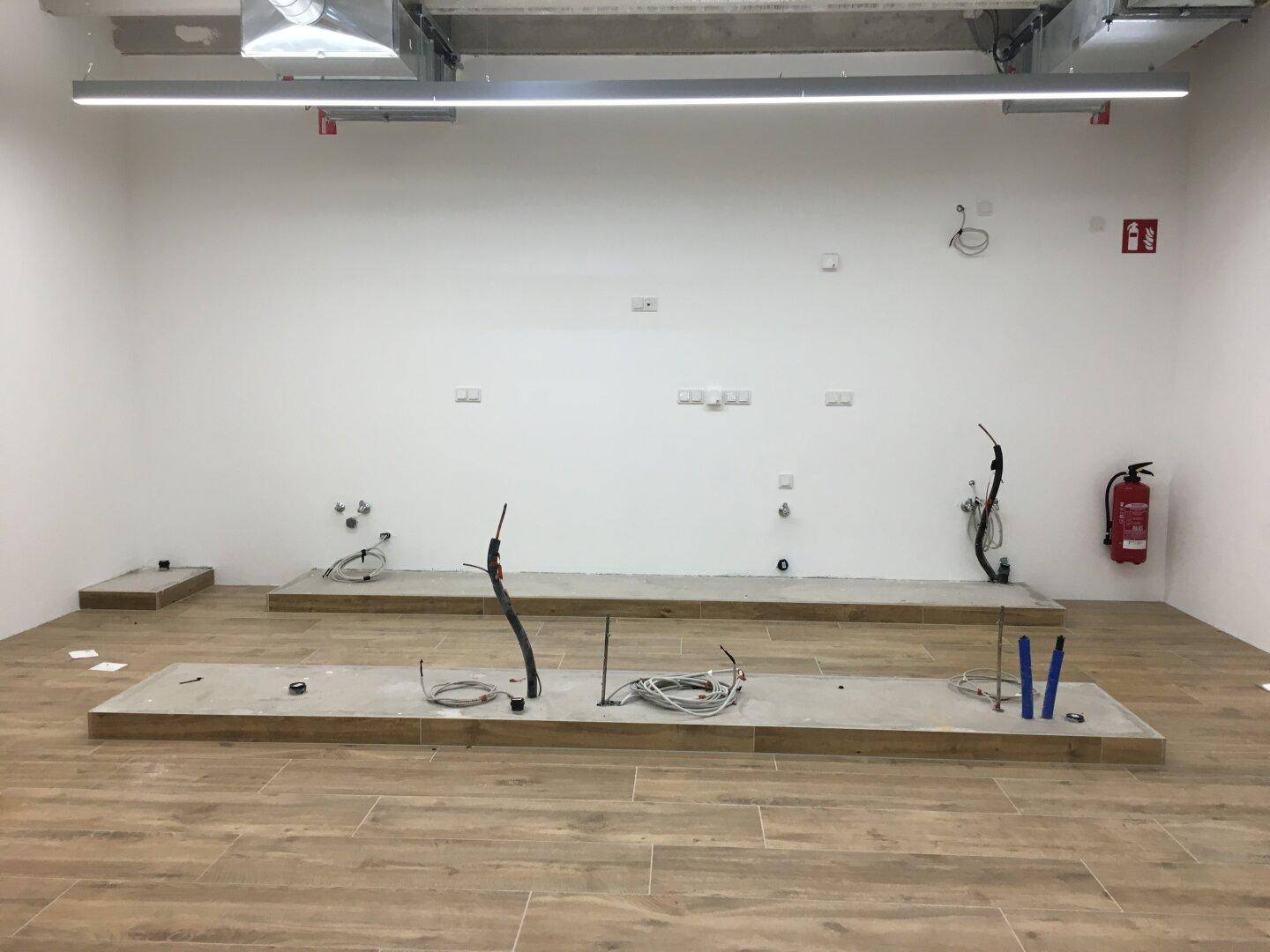 Raum im Bau mit sichtbaren Installationen und Holzoptik-Fliesen, bereit für die weitere Gestaltung.
