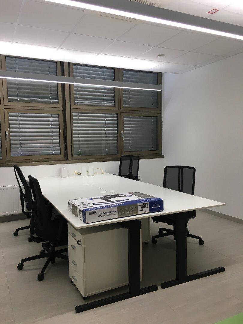 Modernes Büro mit großem Schreibtisch, Bürostühlen und Fenstern mit Jalousien.