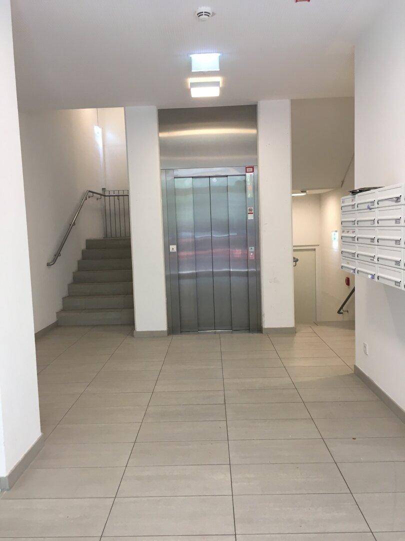 Heller Eingangsbereich mit Aufzug und Treppenhaus, ausgestattet mit Fliesenboden und Briefkästen an der Wand.