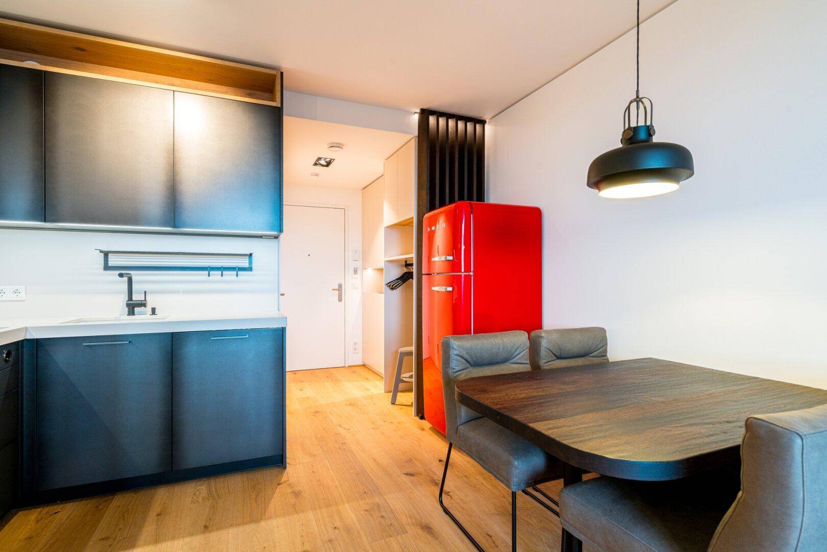 Essbereich mit Holztisch und Stühlen, angrenzend an eine moderne Küche mit rotem Kühlschrank.