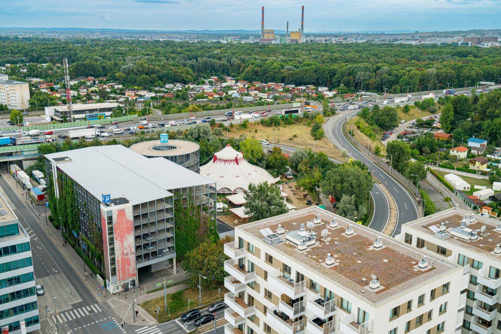 Luftaufnahme einer städtischen Umgebung mit Autobahn, Wald und Wohngebäuden.