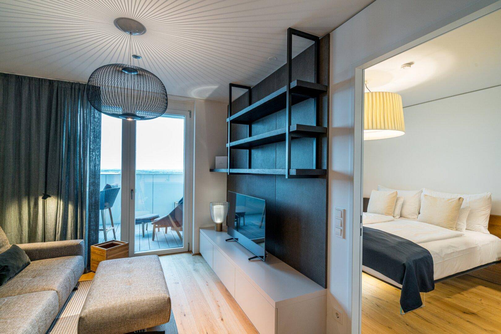 Heller Wohnbereich mit Sofa, Fernseher und direktem Zugang zu einem sonnigen Balkon.