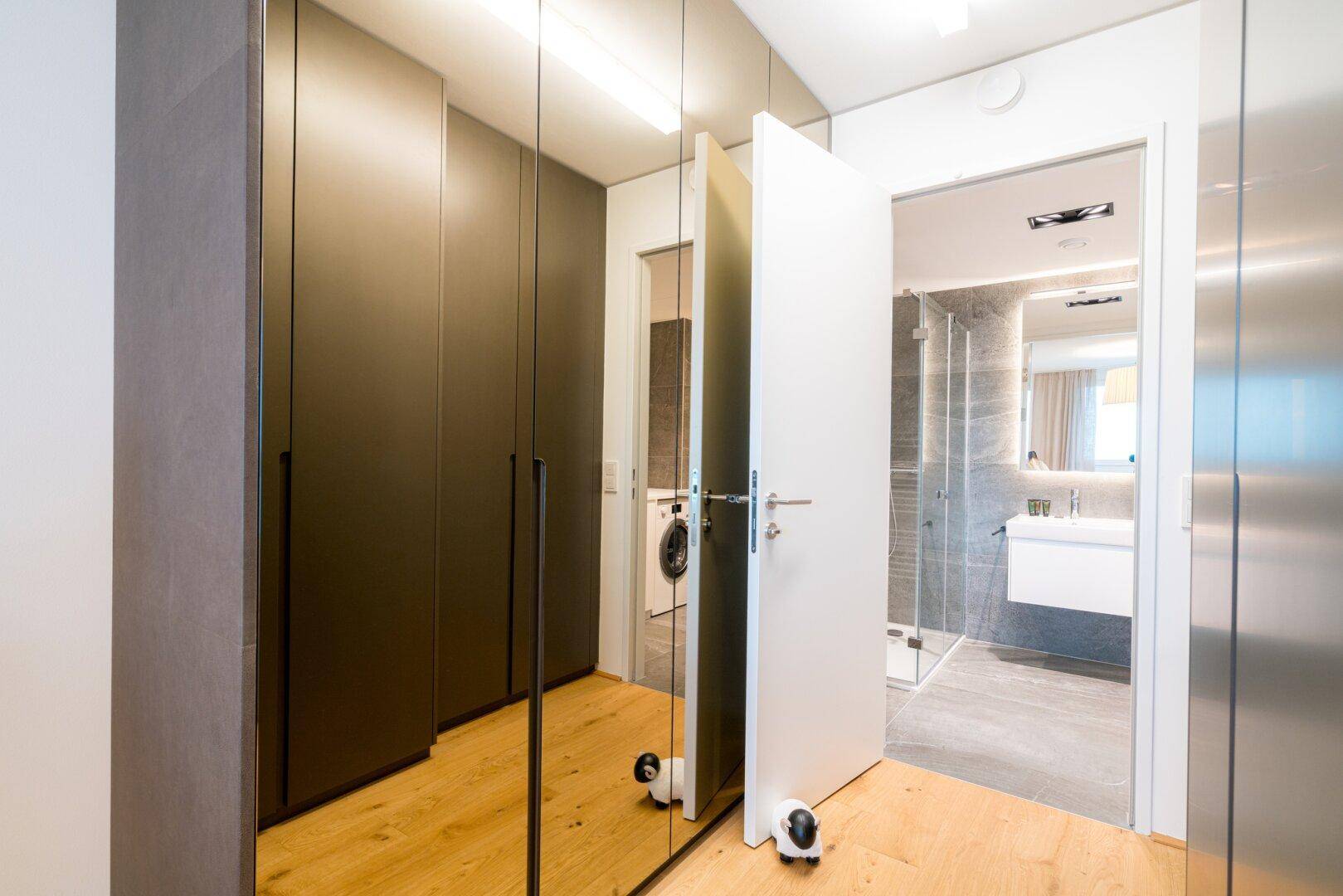 Flur mit Spiegelschränken und Zugang zu einem modernen Badezimmer mit Dusche.