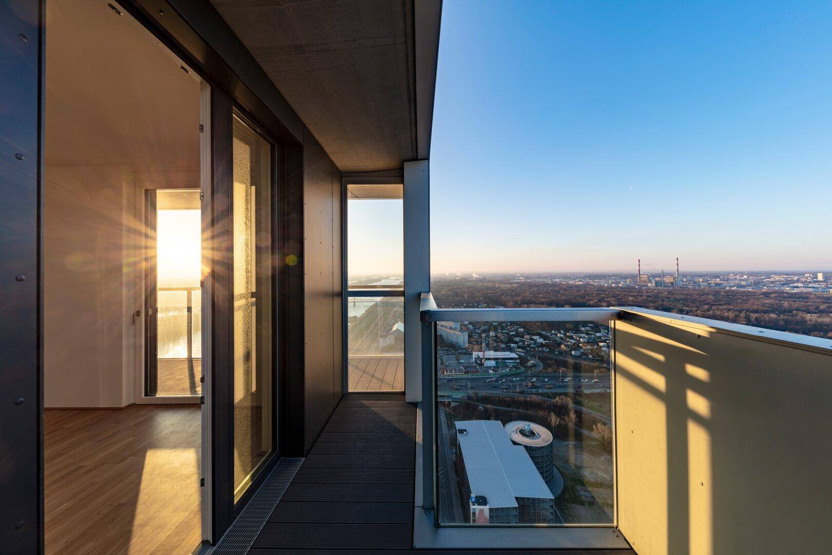 Geräumiger Balkon mit Holzboden und Zugang zu einem hellen Innenraum mit Parkettboden.