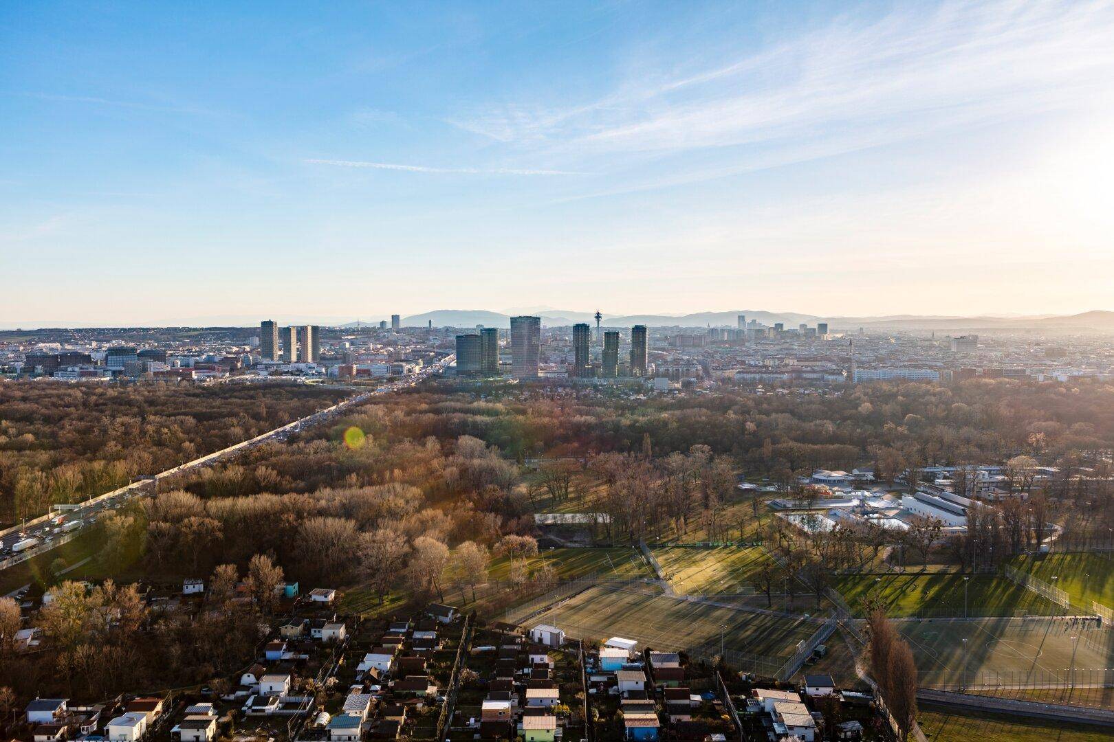 Weitläufiger Blick über die Stadt mit grünen Flächen, Wohngebieten und Hochhäusern unter blauem Himmel.