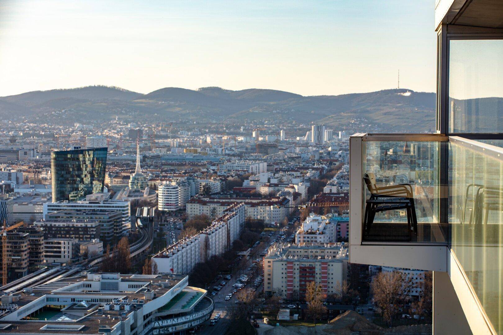 Kleiner Balkon mit Glasbrüstung und Stuhl, bietet einen weiten Blick über die Stadt und die Hügel.