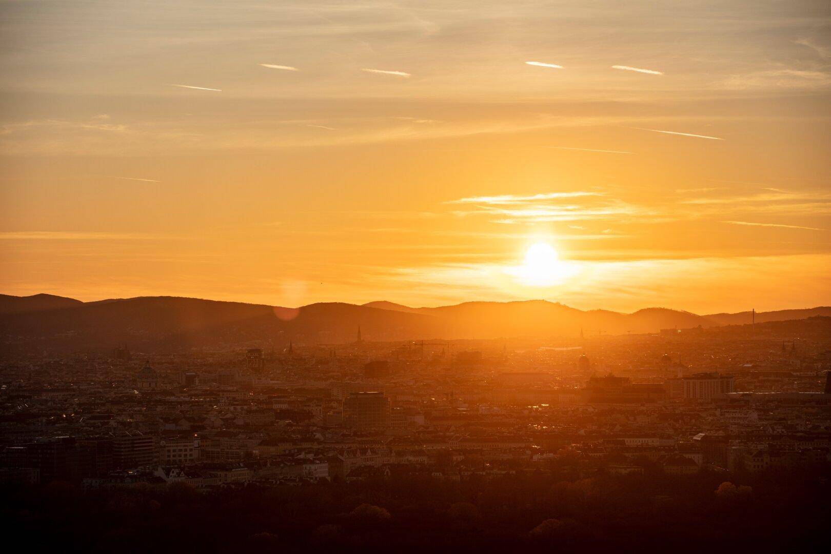 Sonnenuntergang über der Stadt mit leuchtendem Himmel und Silhouette der Berge im Hintergrund.
