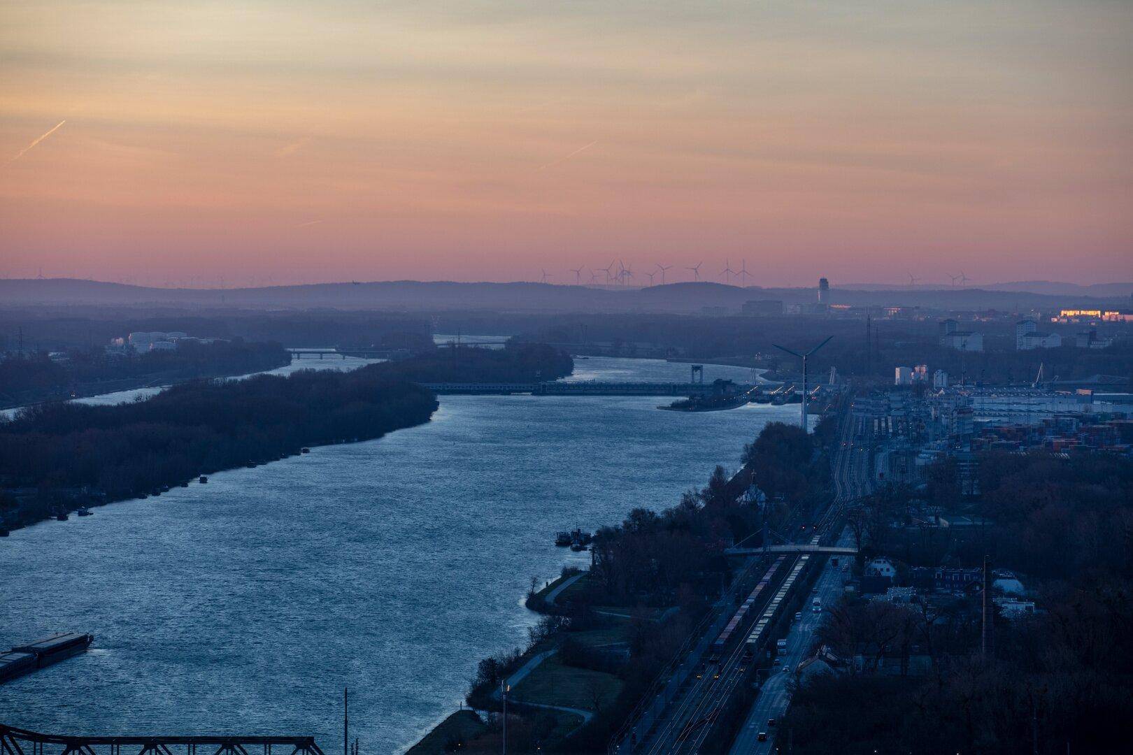 Weitläufiger Blick auf den Fluss mit Brücken und bewaldeten Ufern in der Dämmerung.