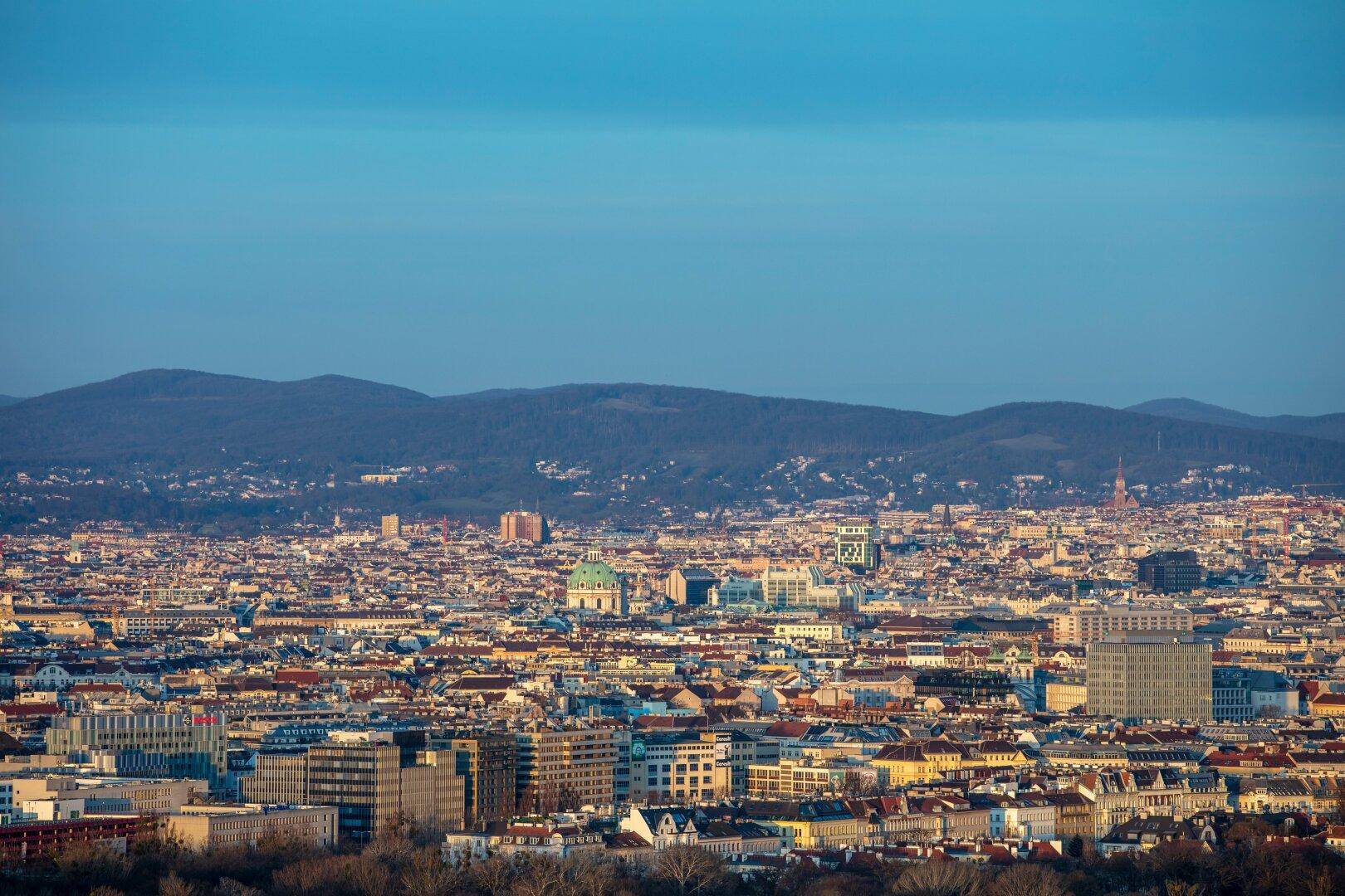 Weitläufiger Blick über die Stadtlandschaft mit Bergen im Hintergrund unter blauem Himmel.