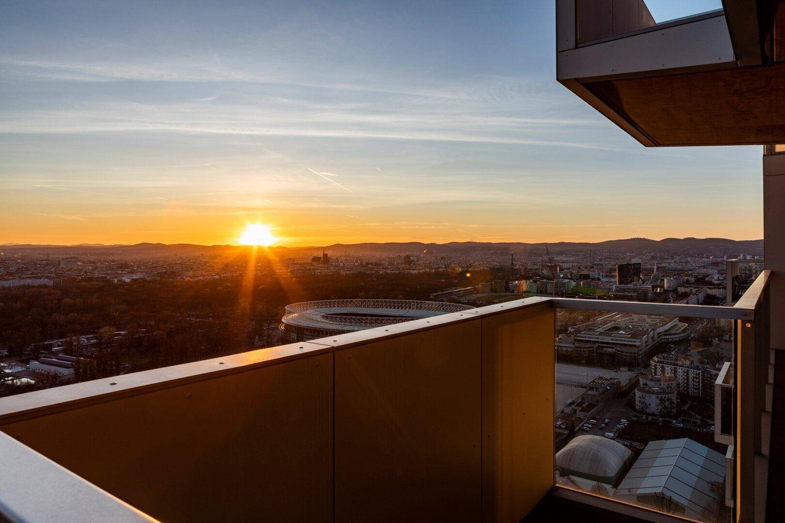 Balkon mit Blick auf den Sonnenuntergang über der Stadt und Sportanlagen.