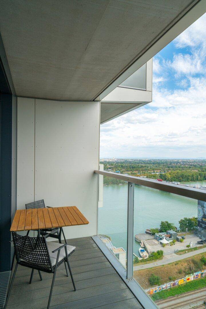 Balkon mit Holzboden, Glasbrüstung und weitem Blick auf den Fluss und die Stadt.