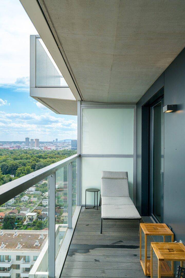 Geräumiger Balkon mit Liegestuhl und Panoramablick über die Stadt und grüne Landschaften.