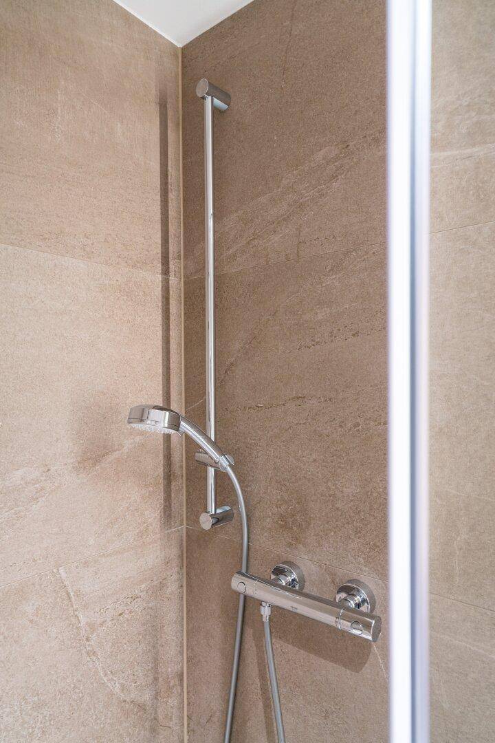 Moderne Duscharmatur in einem gefliesten Badezimmer mit neutralen Farbtönen.