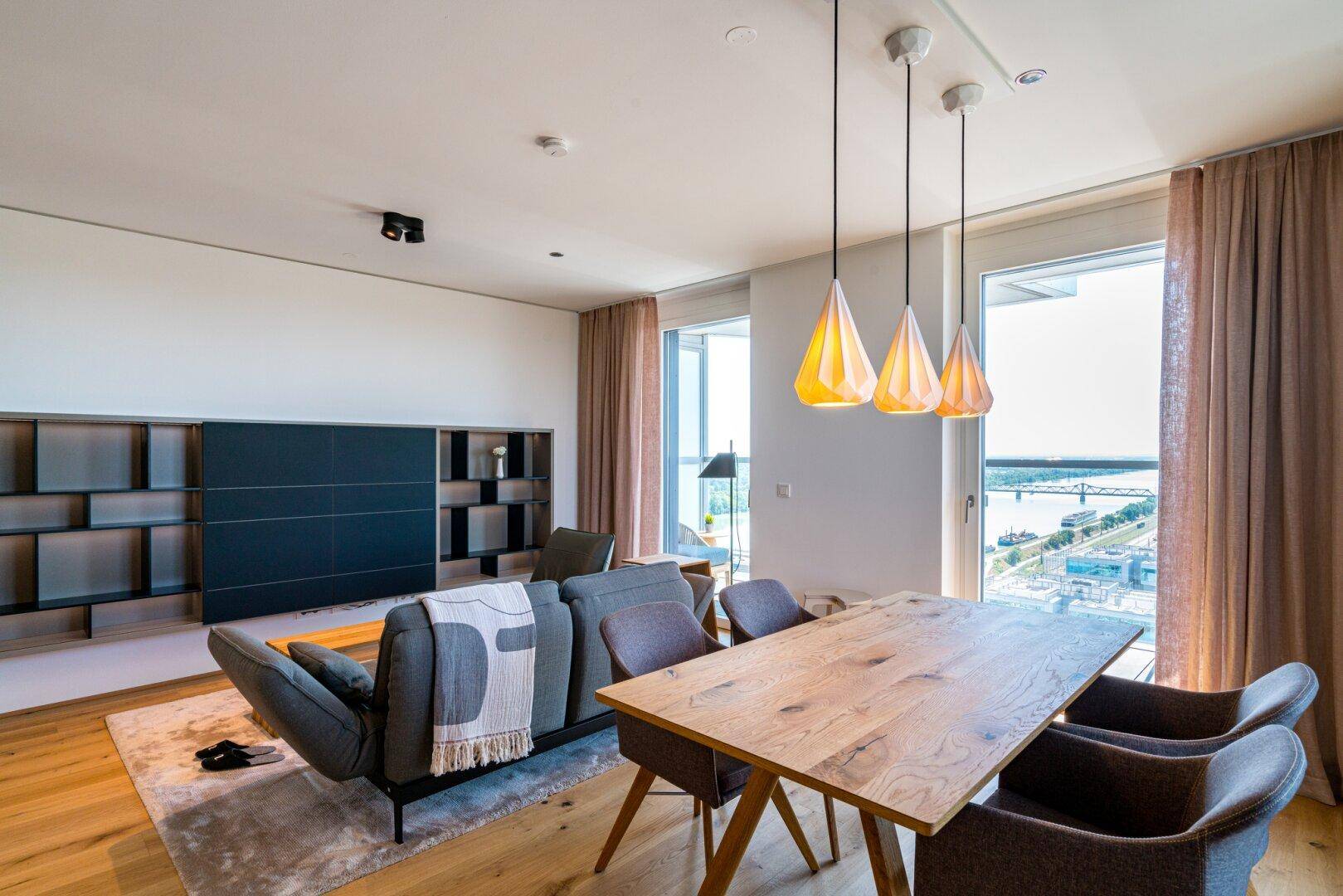 Moderner Wohn-Essbereich mit Holztisch, bequemer Couch und Panoramablick auf die Stadt und den Fluss.