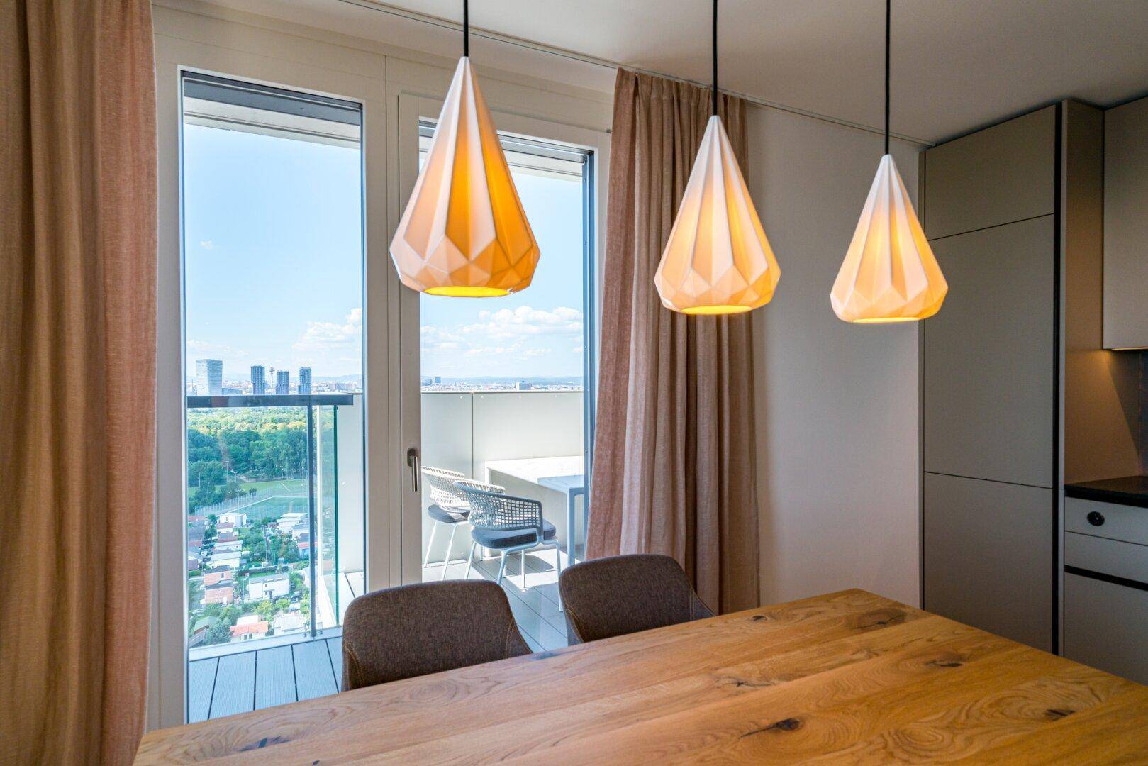 Essbereich mit Holztisch und Zugang zu einem Balkon mit Stadt- und Grünblick.