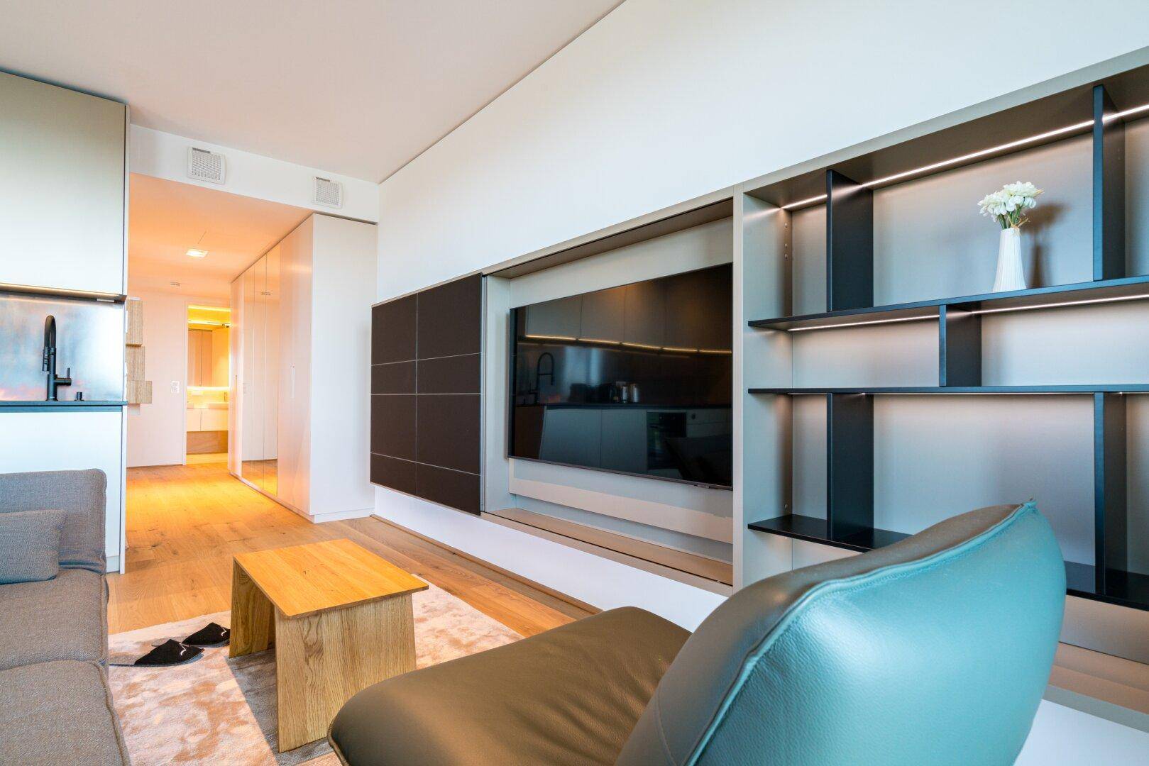 Wohnzimmer mit moderner Medieneinheit, Holzboden und Blick in den Flur.