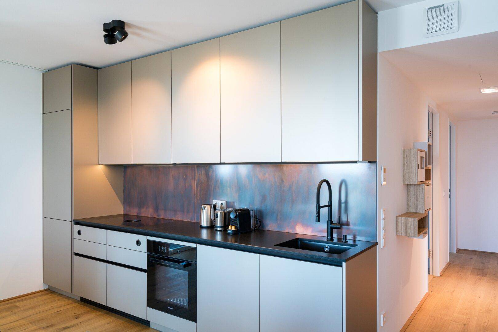 Moderne Einbauküche mit hellgrauen Fronten, dunkler Arbeitsplatte und integriertem Backofen.