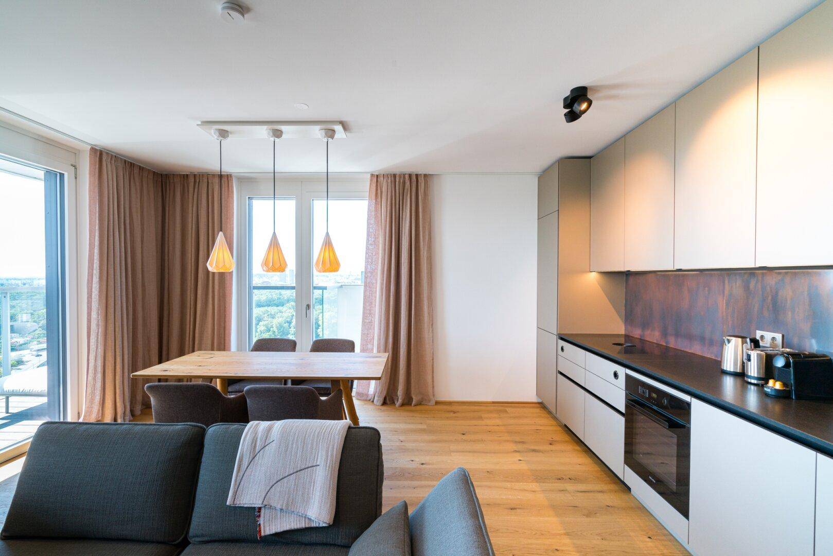 Offener Wohn-Essbereich mit moderner Küche, Holzboden und Zugang zum Balkon.