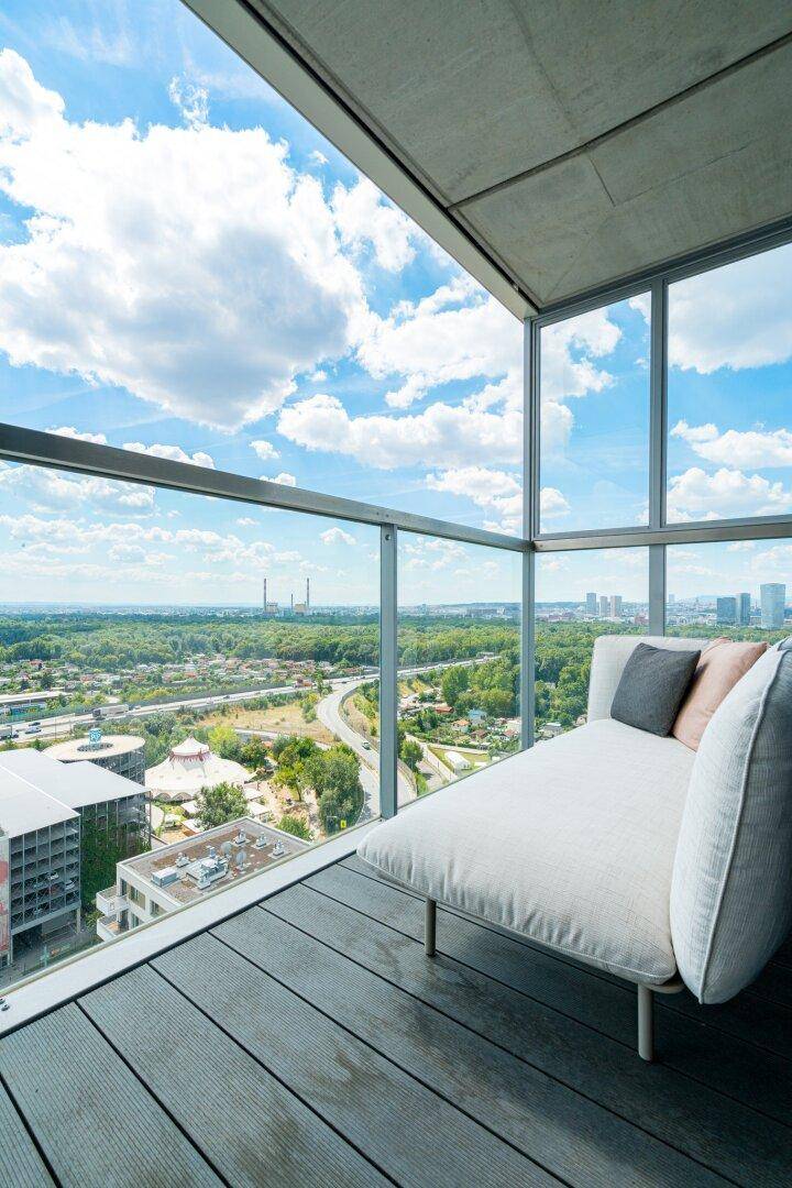 Geräumiger Balkon mit Liege und Panoramablick auf die Stadt und grüne Umgebung.