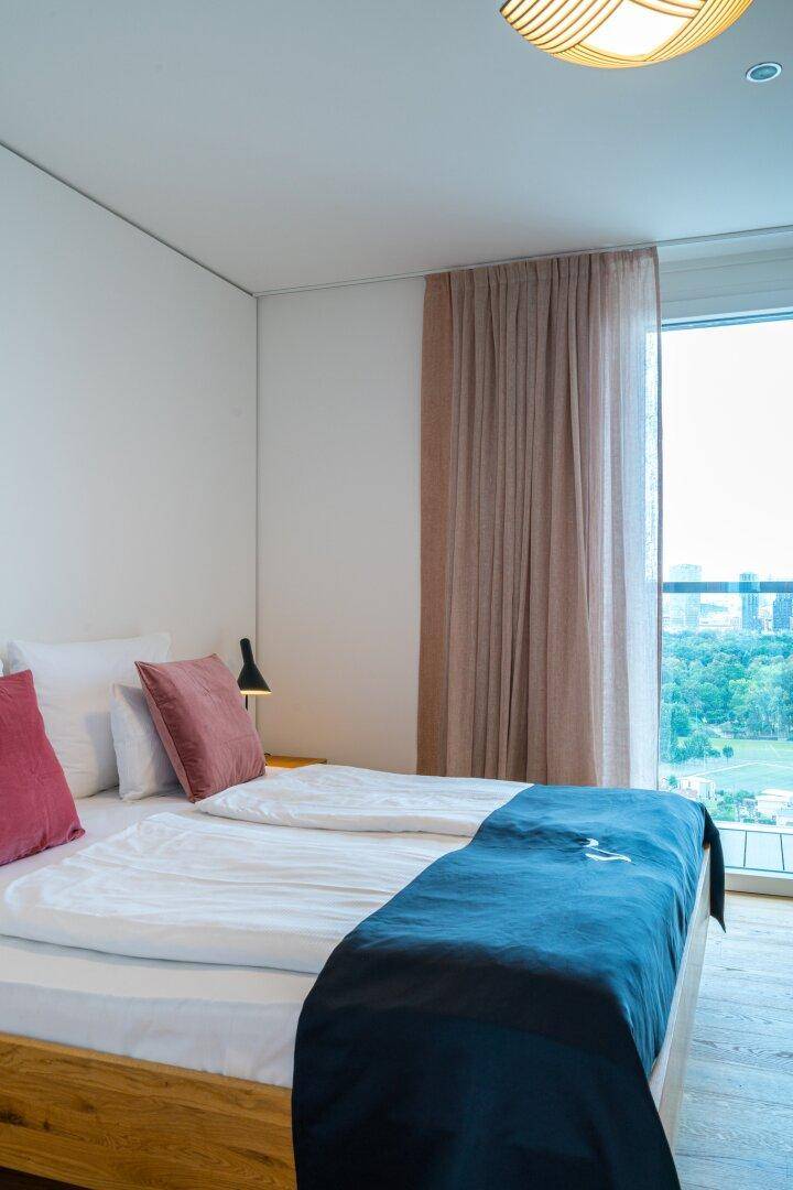 Schlafzimmer mit Doppelbett, Holzboden und großen Fenstern mit Weitblick.