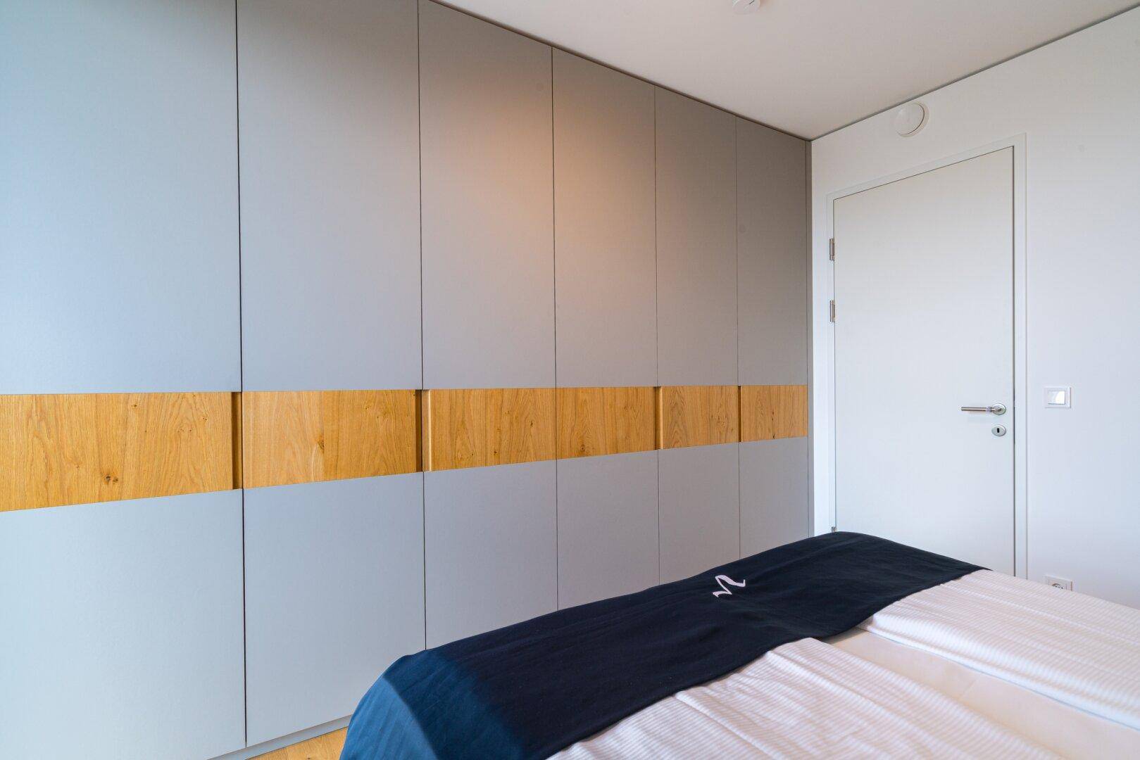 Schlafzimmer mit modernem Einbauschrank in Grau und Holzdetails.