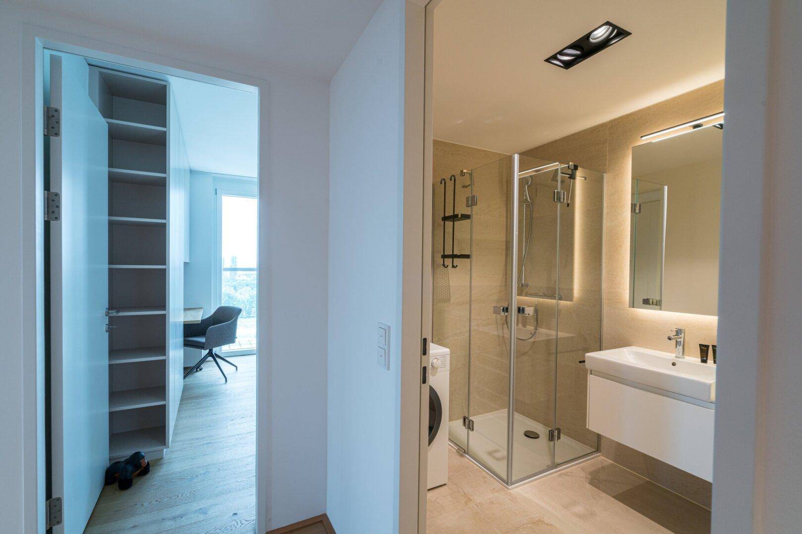 Modernes Badezimmer mit Dusche, Waschmaschine und Zugang zu einem weiteren Raum.