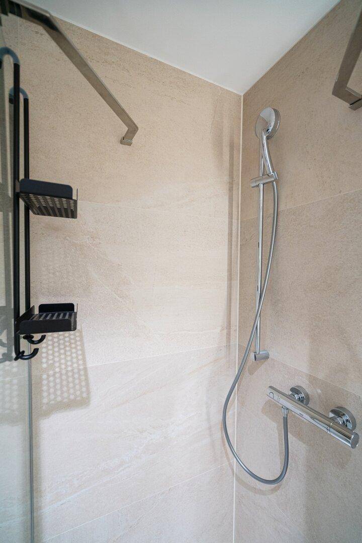 Duschbereich mit moderner Armatur und Ablagen in einem hell gefliesten Badezimmer.