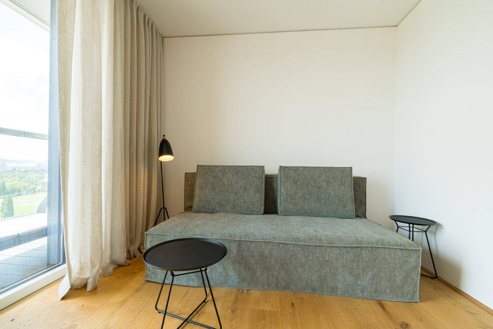 Gemütliches Wohnzimmer mit Schlafsofa, Beistelltischen und großen Fenstern.