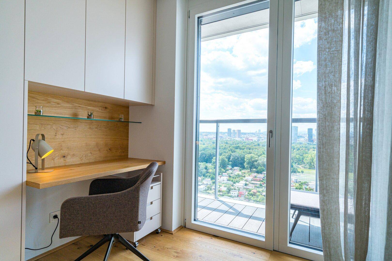 Helles Arbeitszimmer mit Schreibtisch, Einbauschränken und Zugang zum Balkon mit Weitblick.