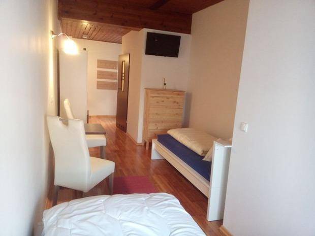 Schlafzimmer mit Einzelbett, Holzkommode und Fernseher, unter einer rustikalen Holzdecke.
