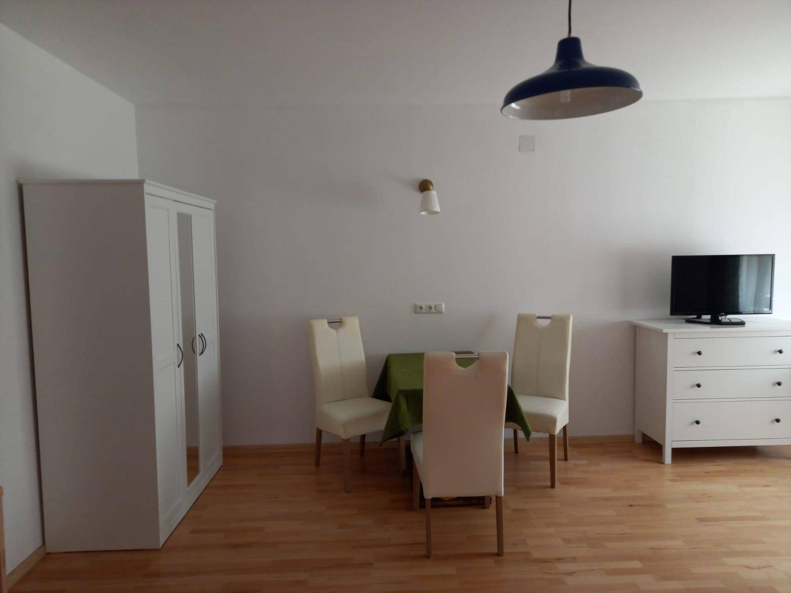 Heller Wohn-Essbereich mit Esstisch, Kleiderschrank und Kommode mit Fernseher.