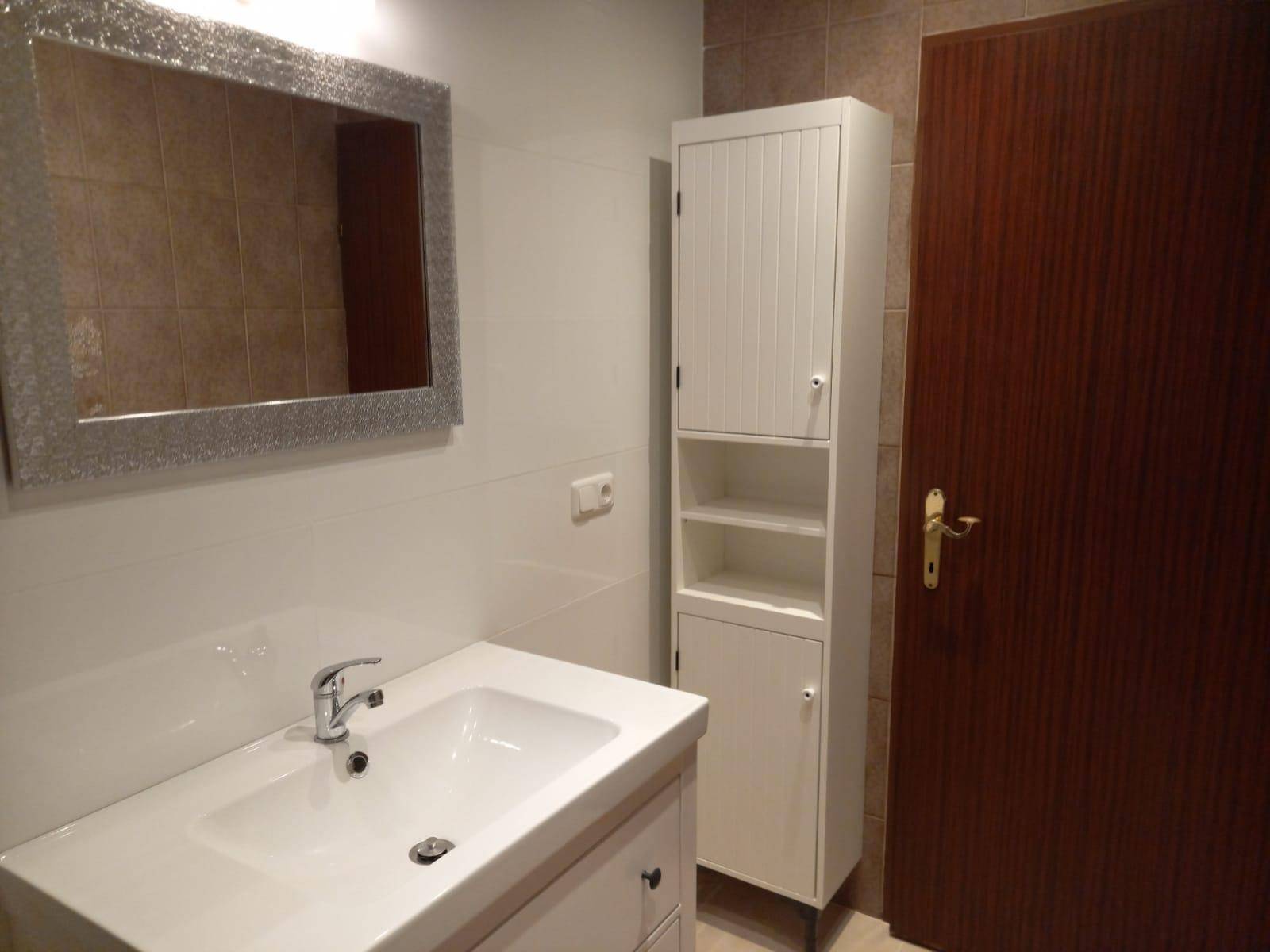 Modernes Badezimmer mit Waschbecken, Spiegelschrank und hohem Stauraumschrank.